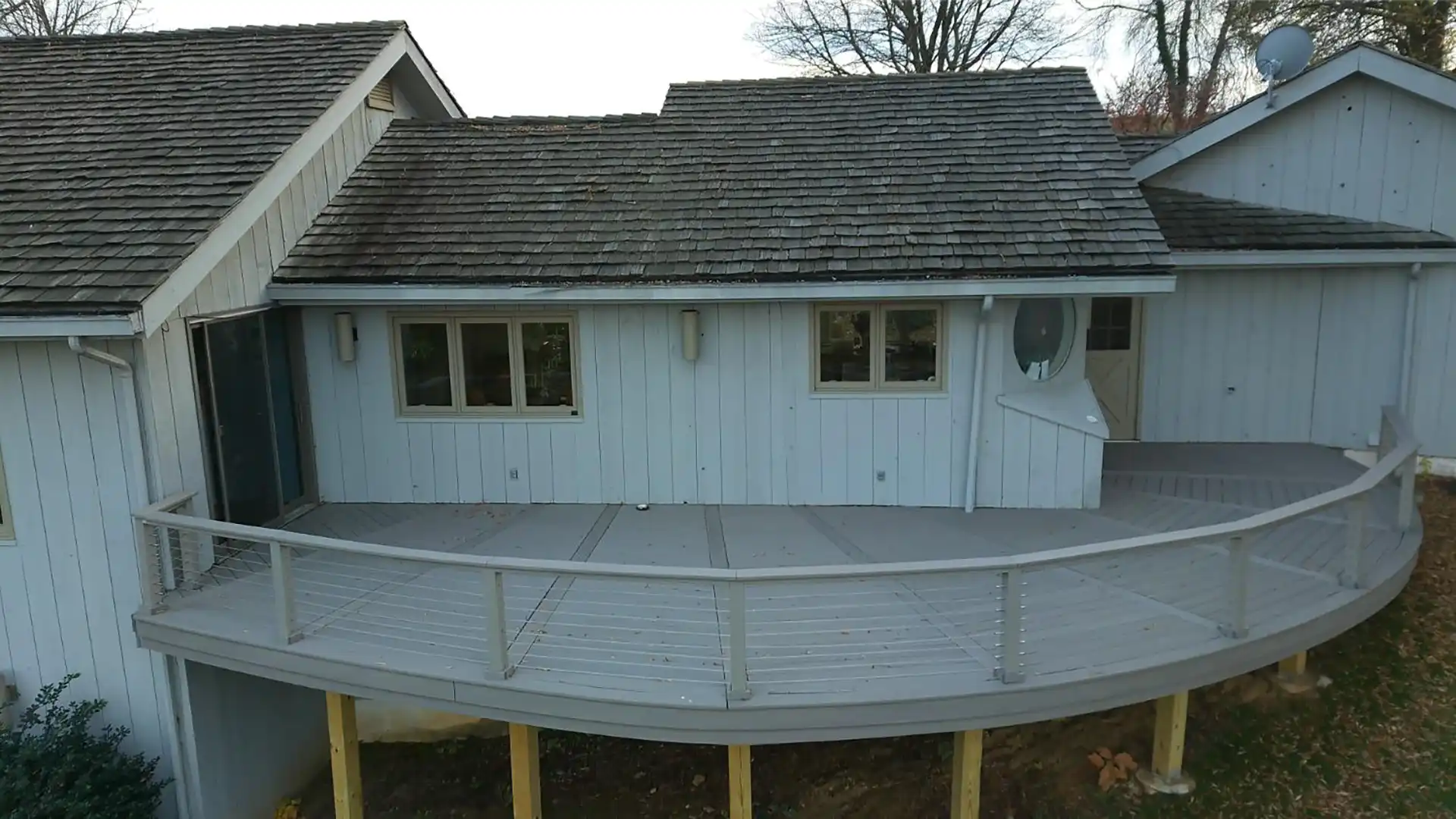 Photo of an elevated, wraparound, composite deck with black metal railing and steps with in-step lighting and a pergola.