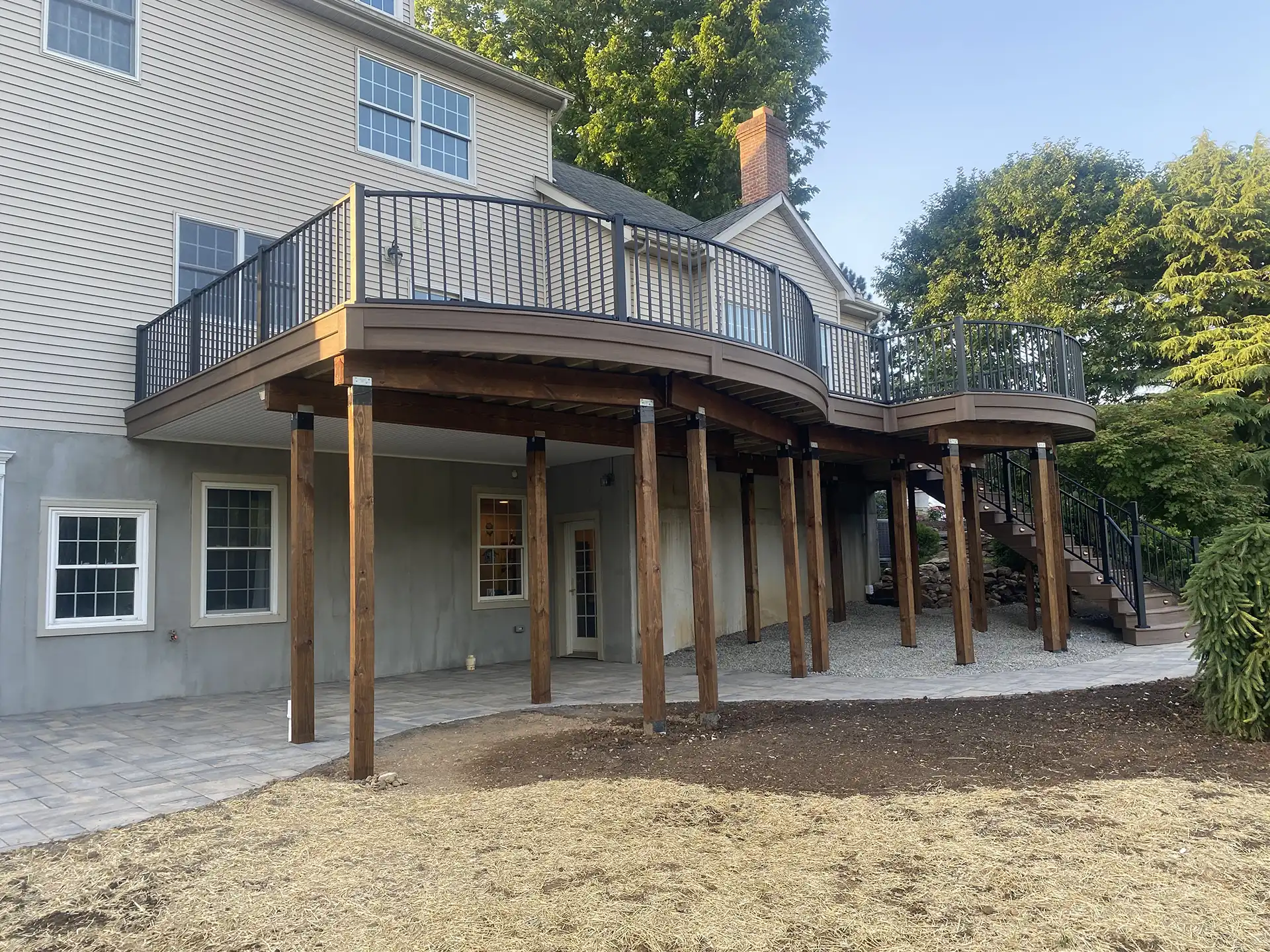 Photo of a custom curved deck with deck railing, steps, and patio underneath