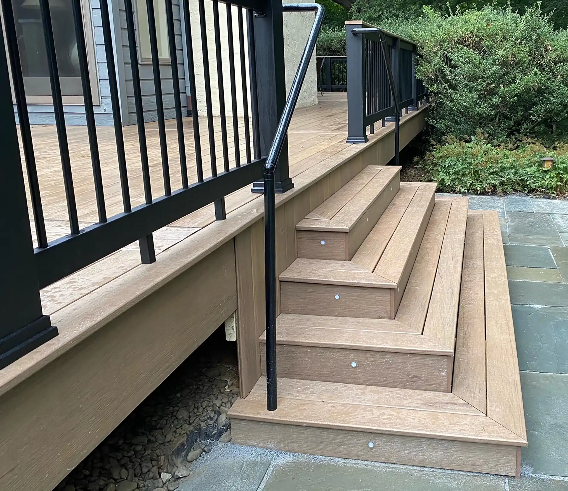 Photo of a custom composite deck with black metal deck railing and steps with in-step lighting - Multi-level Deck Builders and contractor in Avondale, PA