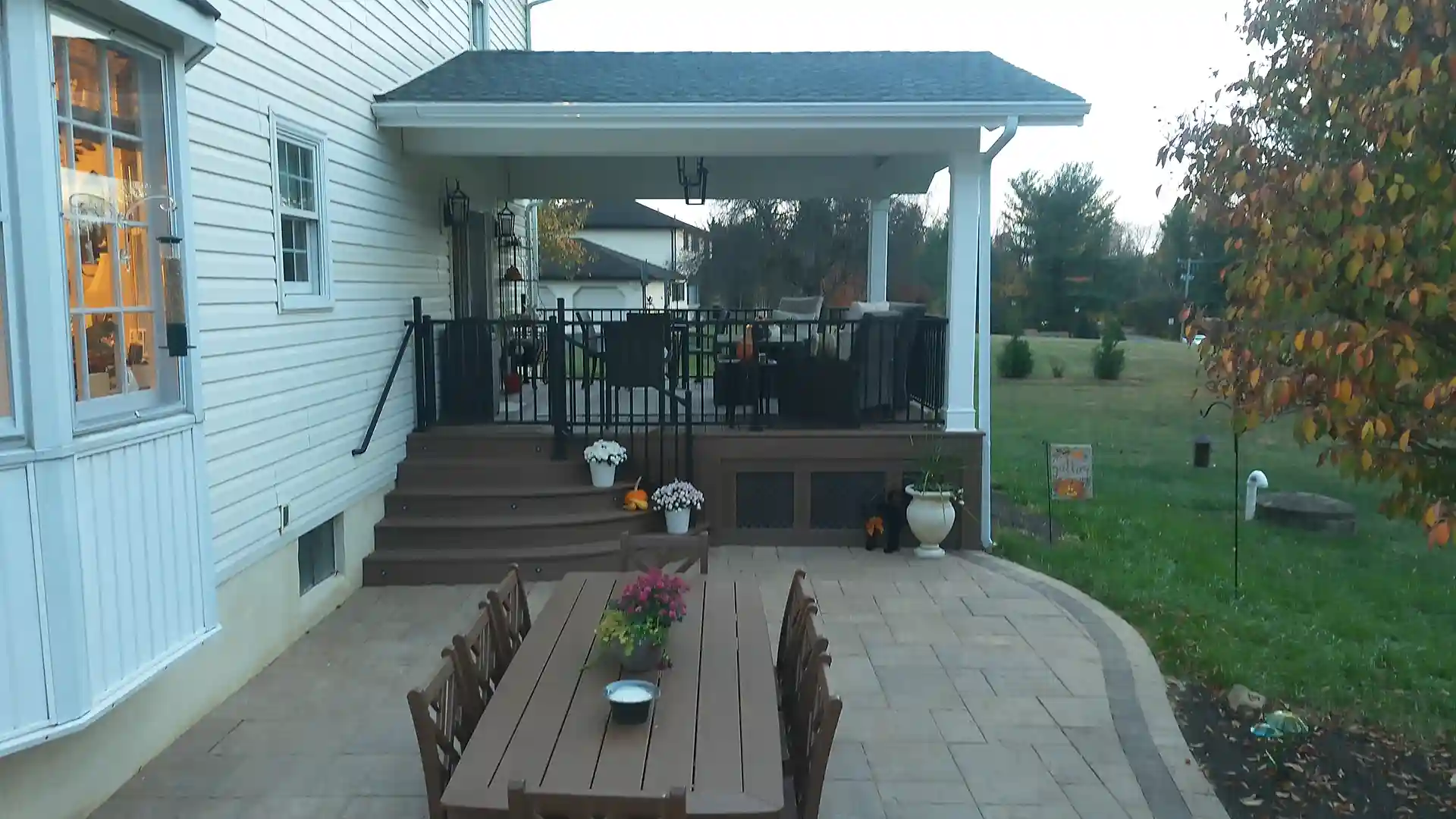 Covered deck with black railings, a dining table on the patio, and a smooth transition to the lawn area.