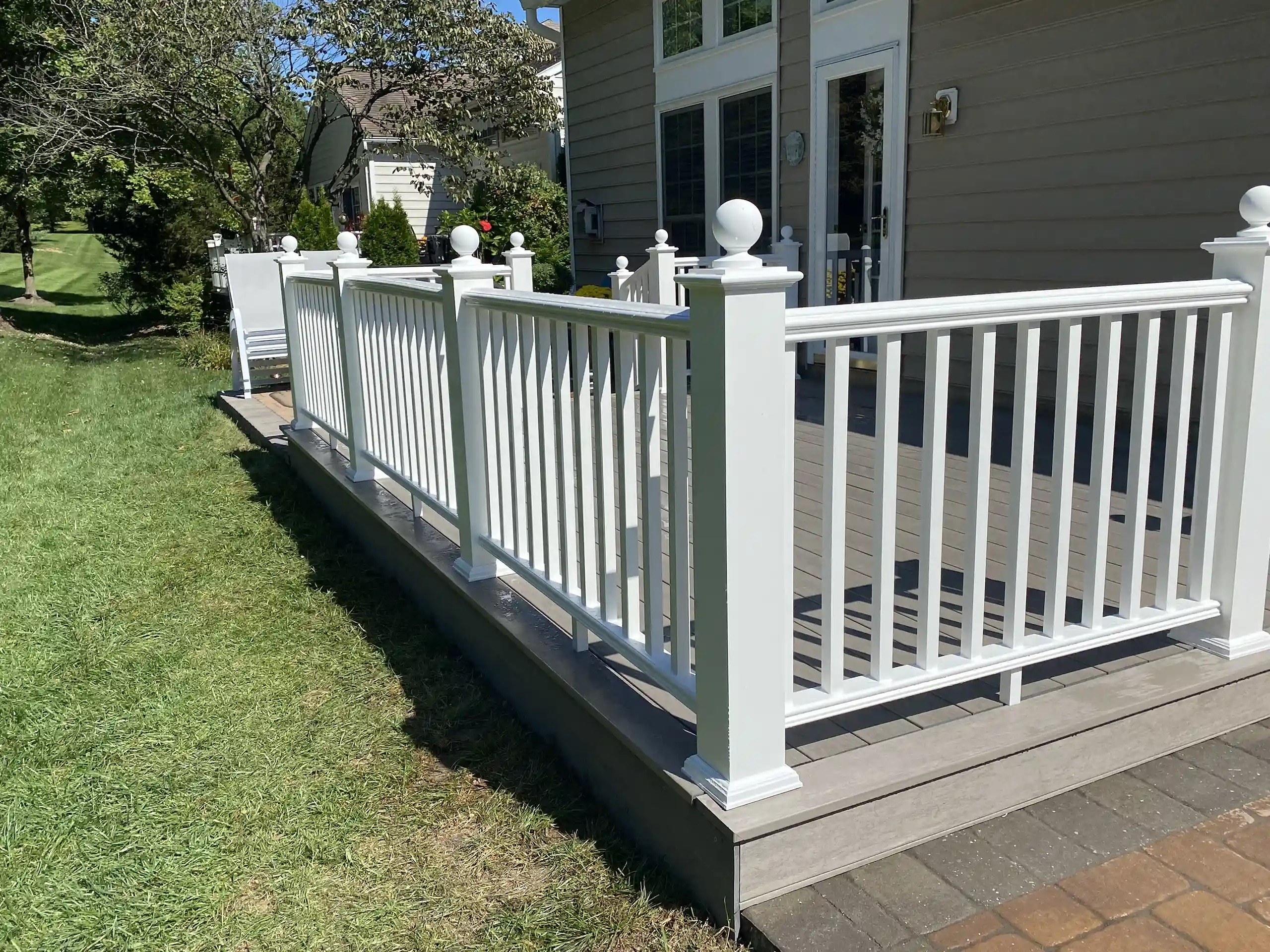 White vinyl railing installed around a raised backyard deck attached to a house.