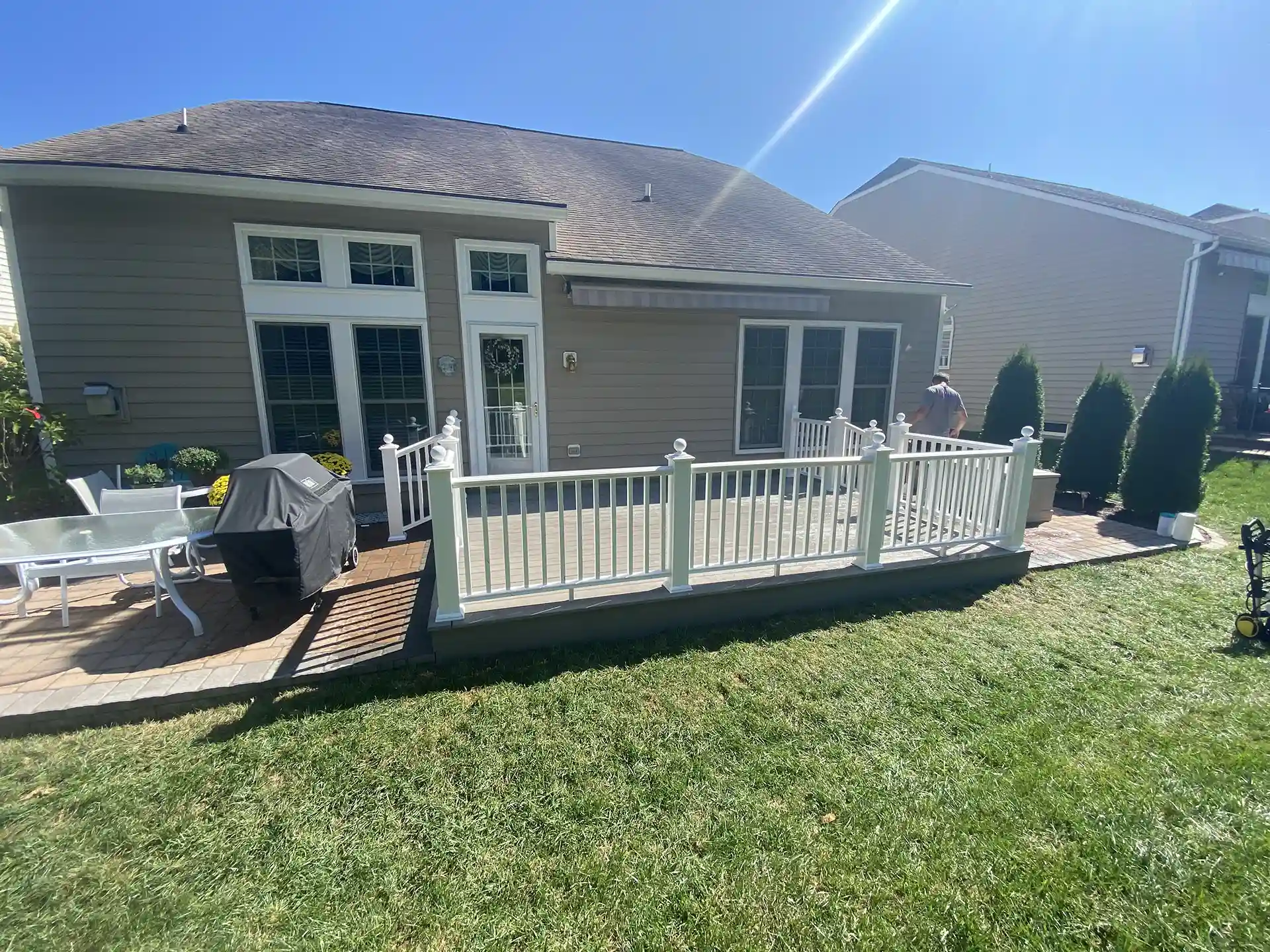 Backyard deck with white vinyl railing attached to a gray house, featuring patio furniture and a grill nearby. 