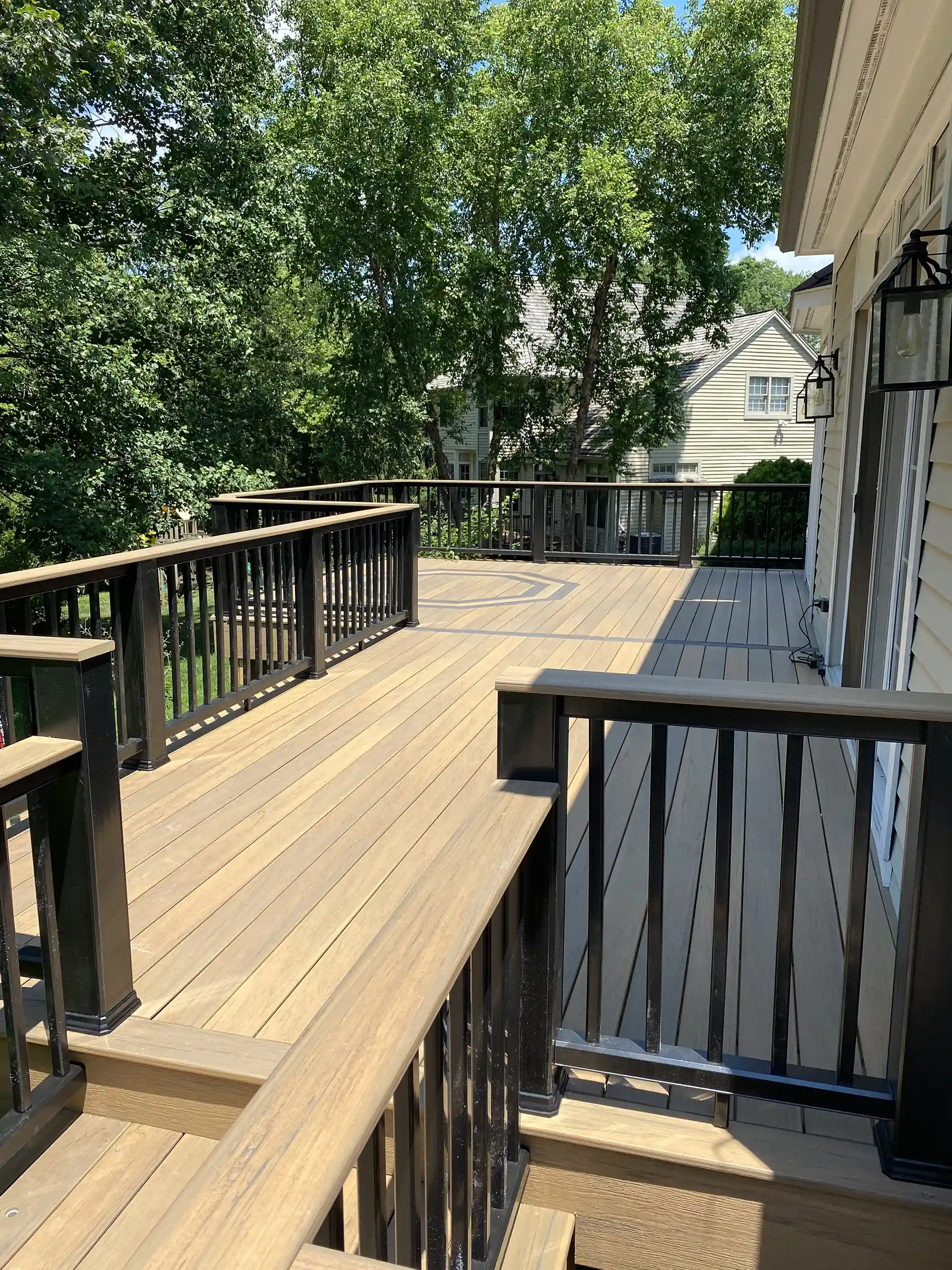 Spacious wood deck with black metal railing surrounded by trees and neighboring houses in the background. 