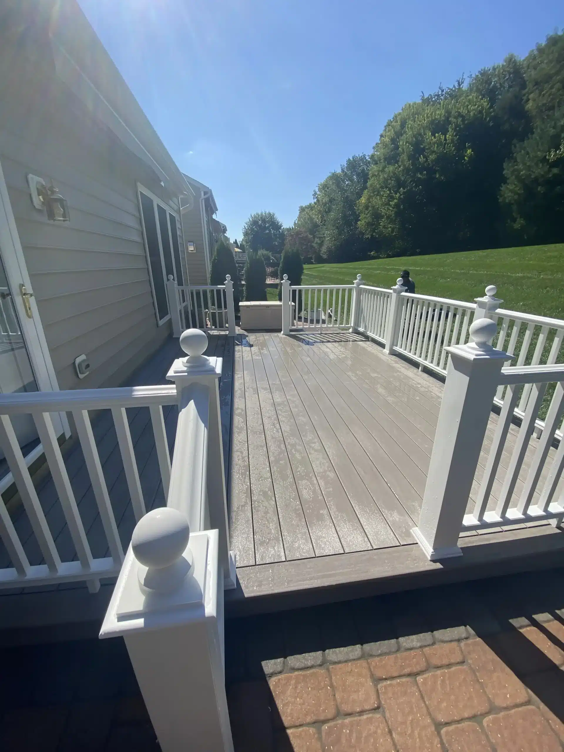 A composite deck with white railings and round posts, featuring a clean and well-maintained surface, with a lush green lawn visible in the background.